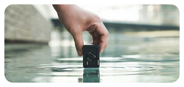 photographer holding Sony RX0 II camera centre of frame touching the water of a pool causing the water to ripple